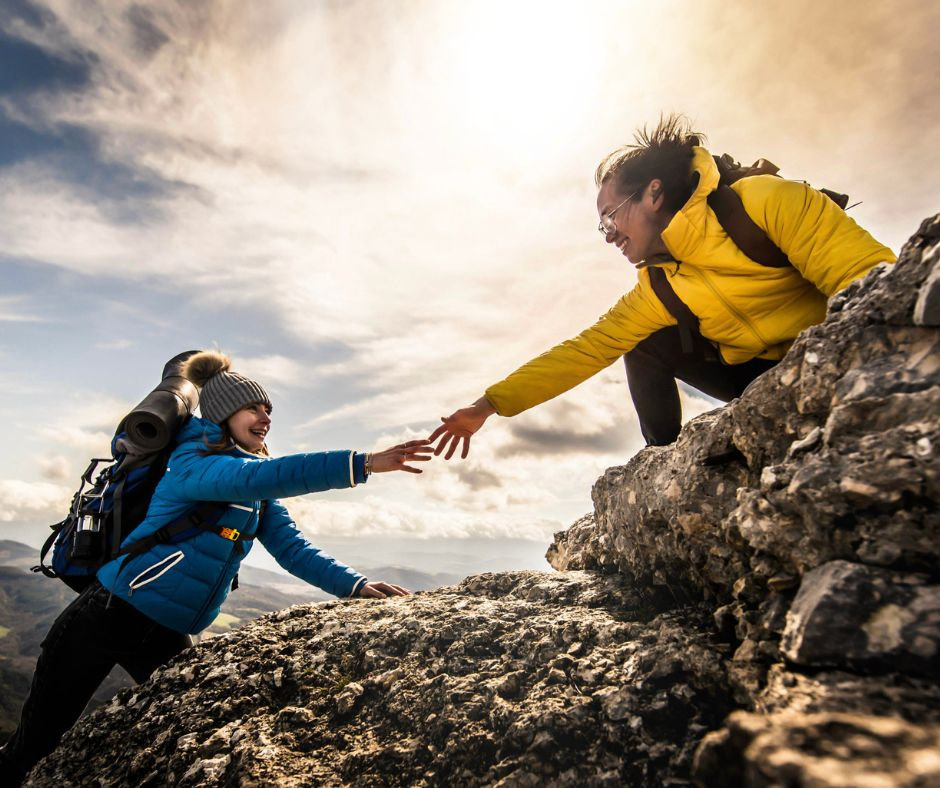 two people climbing a mountain helping each other up